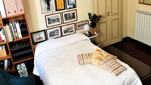 Een netjes ingerichte slaapkamer met een bed, een nachtkastje met een lamp, een boekenplank en ingelijste foto's aan de muur.