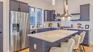 A modern kitchen with a stainless steel refrigerator, a central island with bar stools, and a built-in stove. - 2mi to DT, 4 Private Rooms, Roof Deck Amazing View (Nashville)