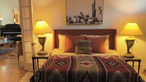 Une chambre à coucher avec un lit, deux lampes de chevet, une couvre-lit à motifs, une plante en pot fixée au mur et une porte donnant sur une autre pièce.