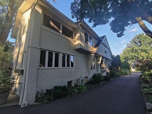 Ein zweistöckiges Haus mit geneigtem Dach, großen Fenstern und einer gepflasterten Auffahrt.