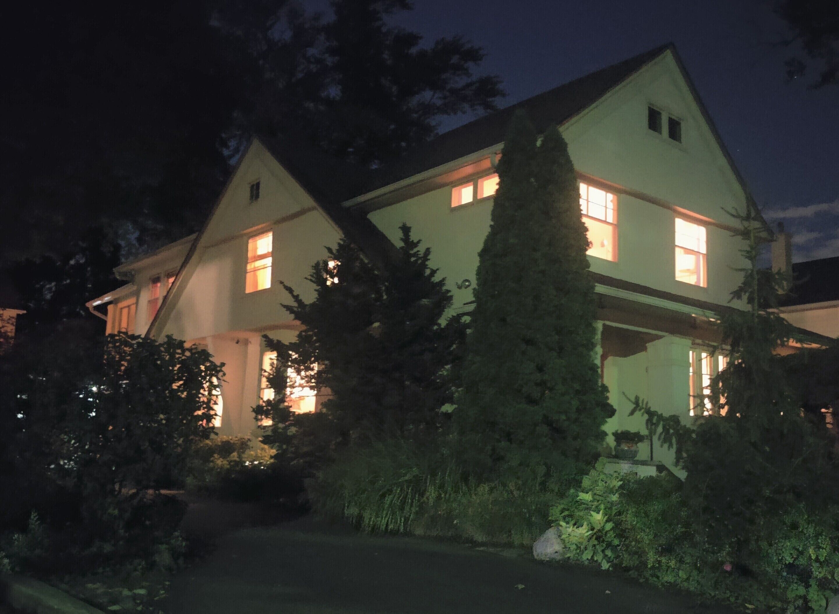 Ein zweistöckiges Haus mit einer sichtbaren Veranda und einem großen immergrünen Baum im Vordergrund.