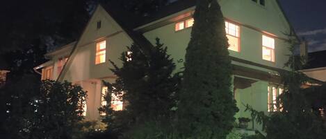 Una casa de dos pisos con un porche delantero visible y un gran abeto en primer plano.