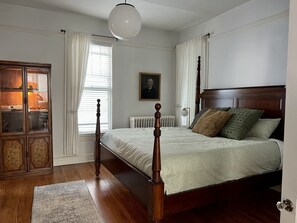 Ein Schlafzimmer mit einem hölzernen Himmelbett, einem Heizkörper, einem Schrank mit Glastüren und einem Porträt an der Wand.