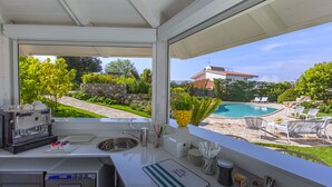 Una cocina con cafetera, lavamanos y vistas a un patio trasero con piscina y mobiliario exterior.