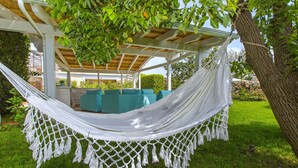 Una hamaca bajo una pérgola con vistas a un jardín y mobiliario exterior.