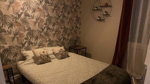 A bedroom with a bed, patterned wall, small bedside table, and a wall-mounted shelf.