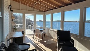 Ein sonnendurchflutetes Zimmer mit großen Fenstern und Blick auf ein Gewässer, das ein Tisch und Stühle sowie eine Aussicht auf Wasser und Bäume bietet.