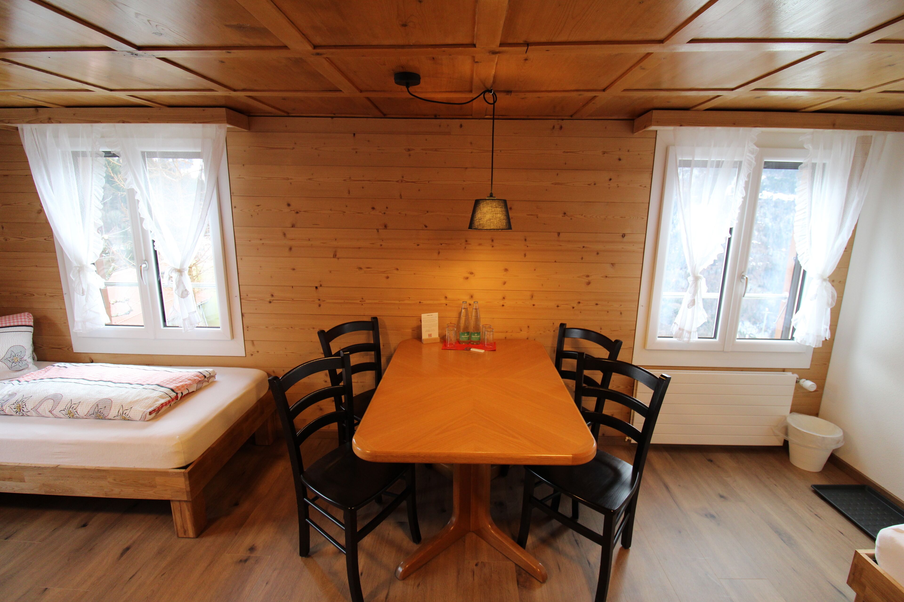 Una habitación con paneles de madera, una cama, una mesa con sillas y una lámpara colgante.