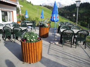 Un espace extérieur aménagé avec des chaises et des tables vertes, entouré de jardinières en bois ornées de fleurs.