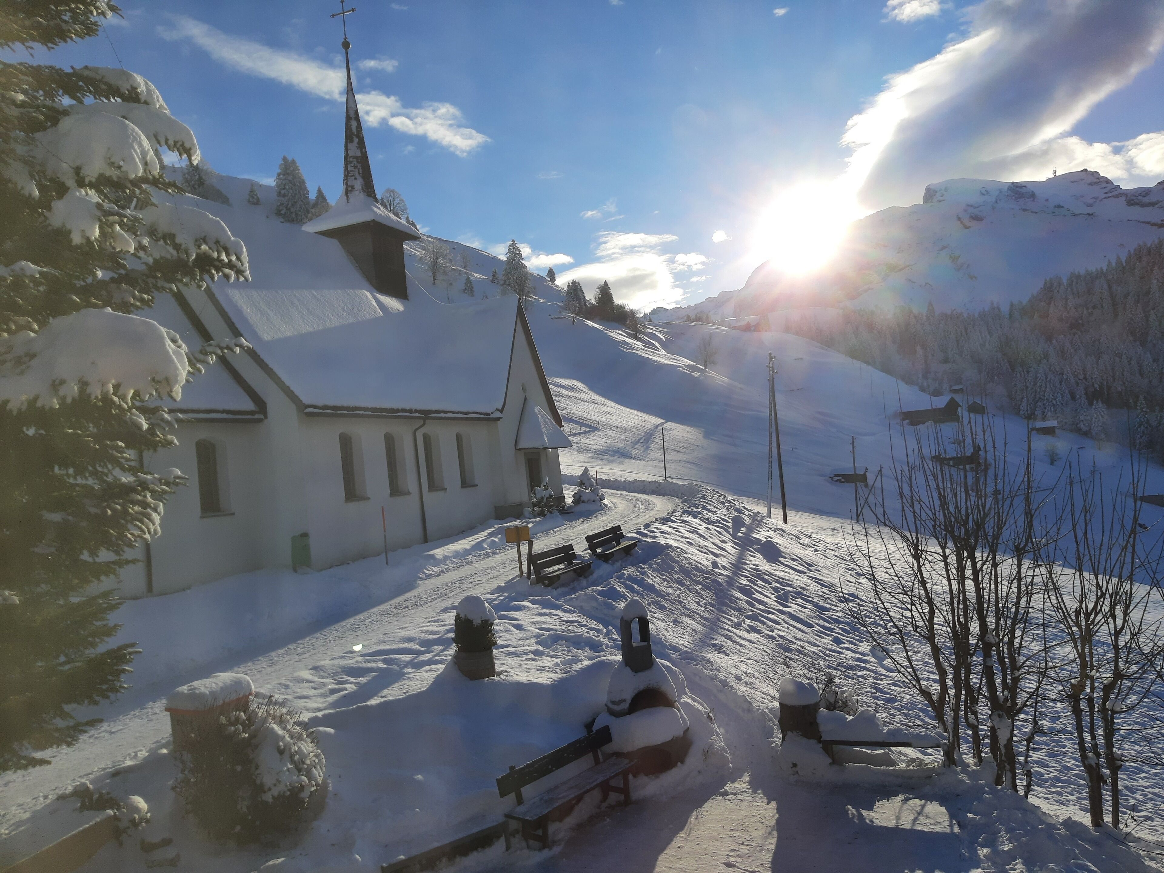 A snow-covered church with a steeple, benches, and a clear sky.