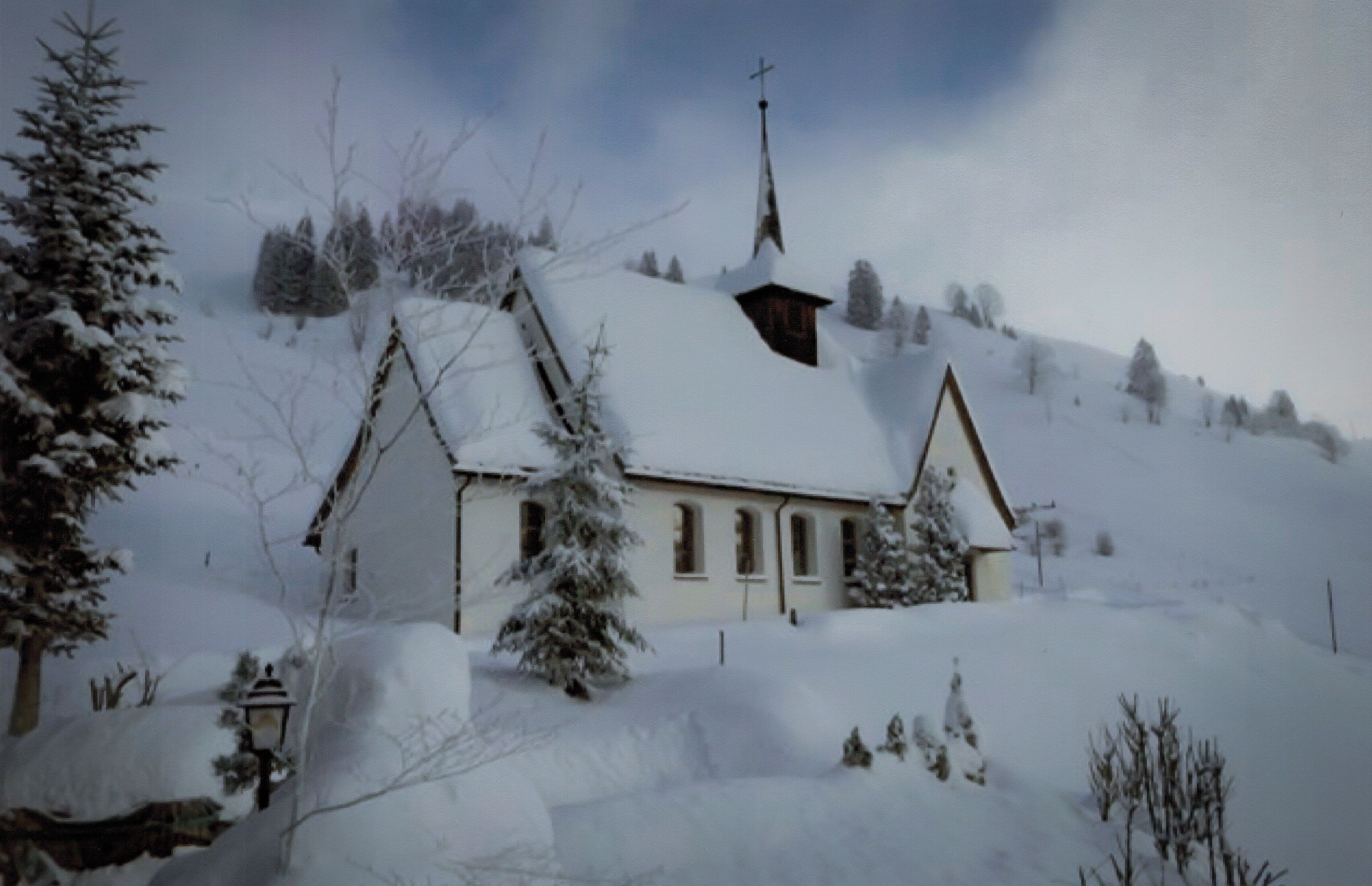 A snow-covered church with a steeple, surrounded by trees and a snowy landscape.