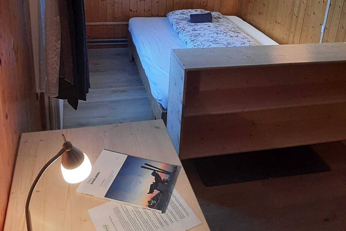 A small, cozy room with wooden walls, a bed, a desk with a lamp, and a TV mounted on the wall.