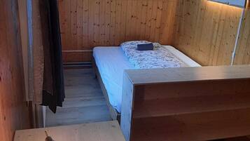 Ein kleiner, gemütlicher Raum mit Holzwänden, einem Bett, einem Schreibtisch mit Lampe und einem an der Wand befestigten Fernseher.