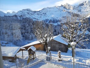 Un paysage de montagne enneigé, avec une cabane en bois et un arbre recouvert de neige au premier plan.