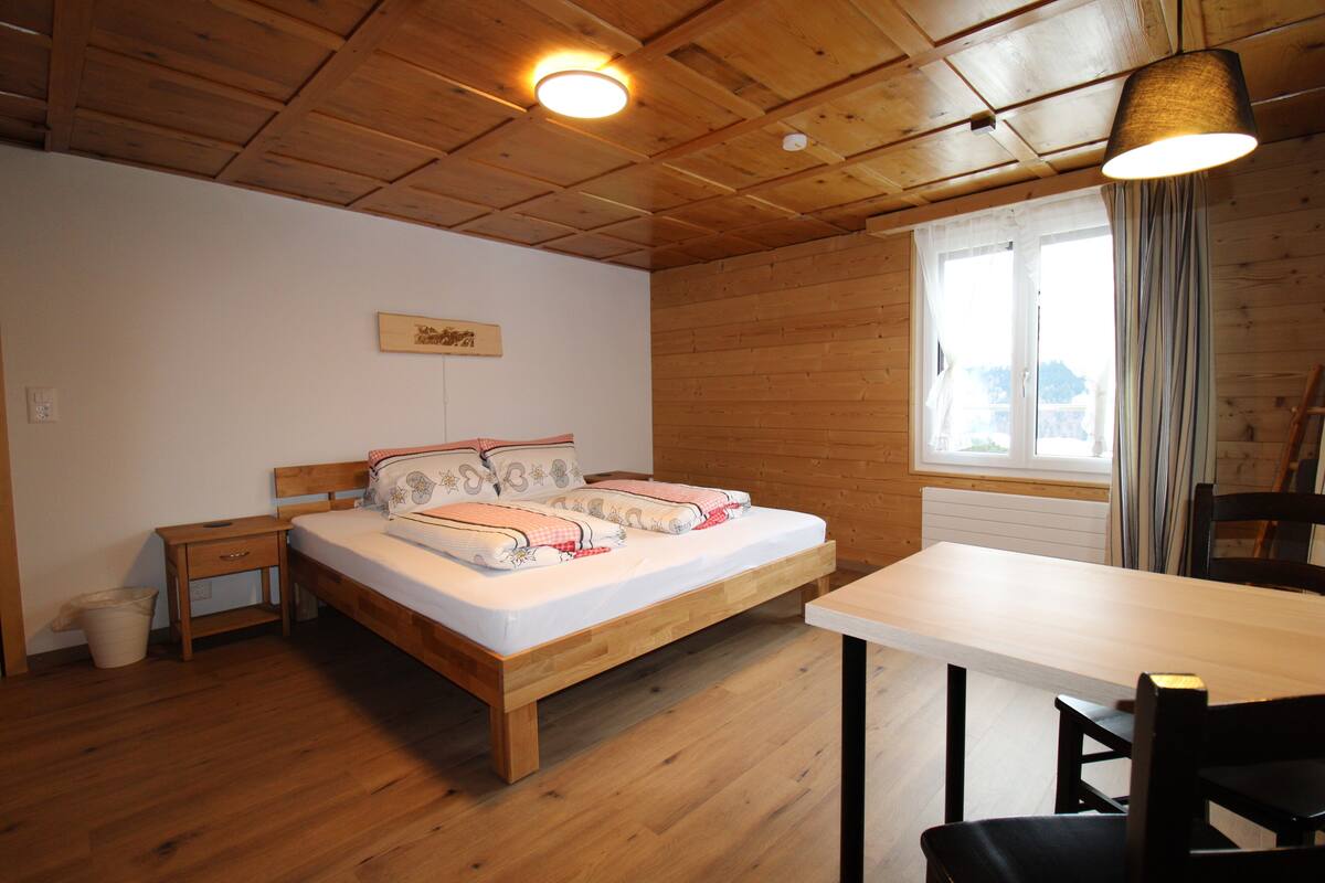 A wooden-paneled room with a bed, a table, and a window with curtains.