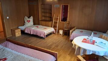A cozy room with two beds, a small table, and a chair. There is a ladder and a shelf unit.