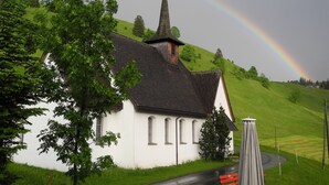 A white church with a pointed steeple and a rainbow in the background. - Gasthaus Schwand (Engelberg)