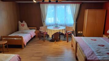 A cozy room with two single beds, a wooden table with chairs, a wardrobe, and a window with curtains.