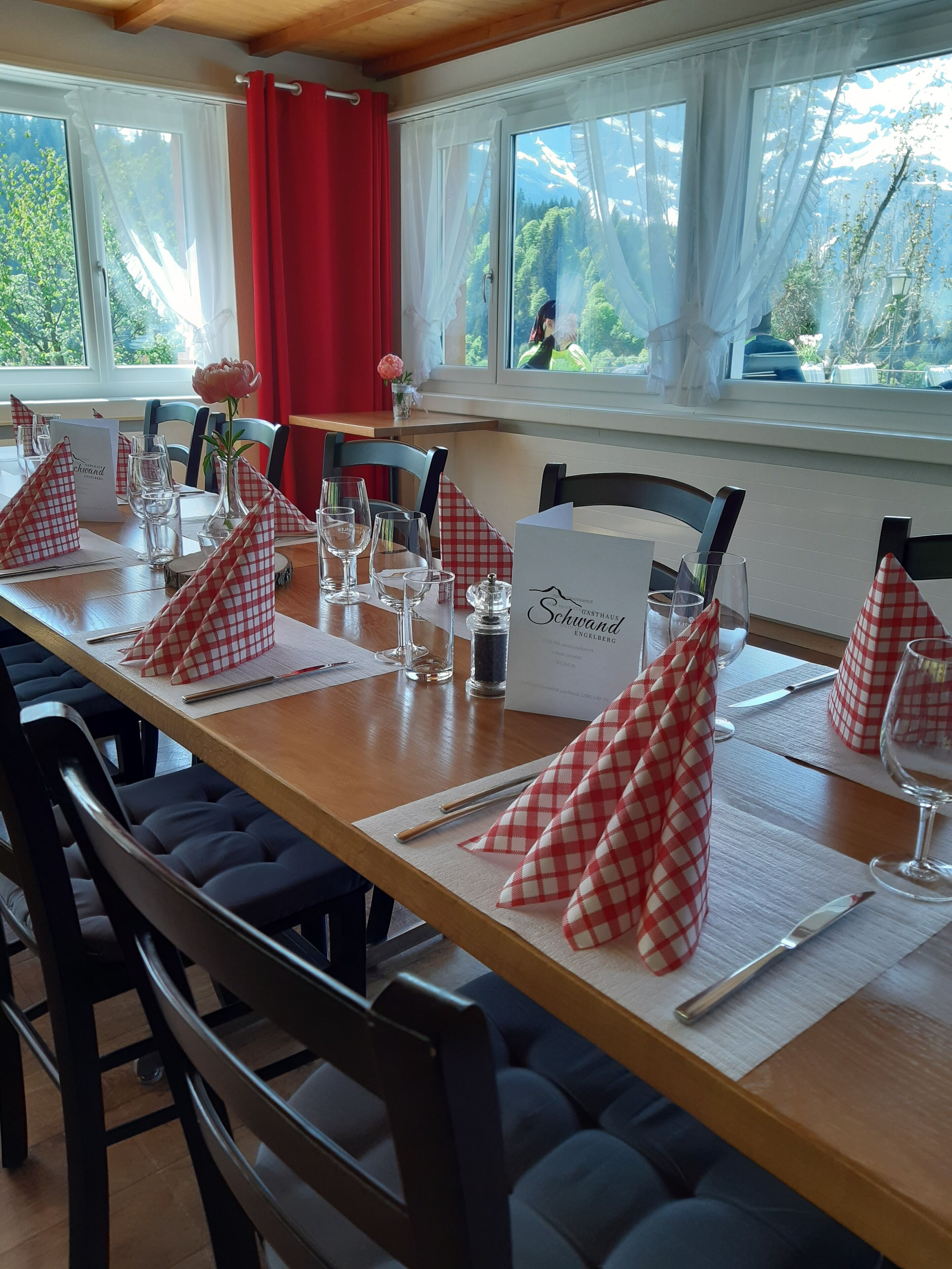 Una mesa de comedor dispuesta con servilletas a cuadros rojos y blancos, vasos transparentes y una carta.