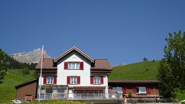Un bâtiment à deux étages, doté d’un toit en pente, de volets rouges et d’un balcon.
