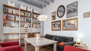 A living room with a black leather sofa, red chairs, a white table with a vase, and a bookshelf filled with books. - Apartament Sweet Home in Cádiz (Cádiz)