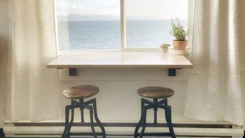 Um quarto com uma janela grande, dois banquinhos de madeira e um vaso com planta no parapeito.