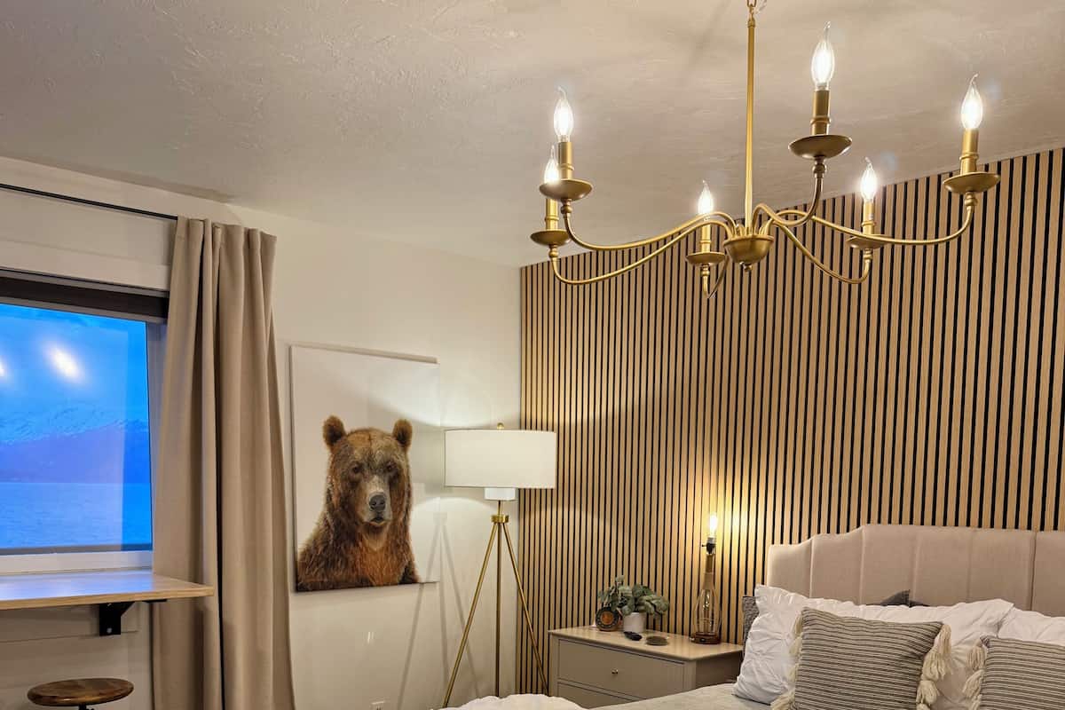 Ein Hotelzimmer mit einem großen Bett, einer Bär-Dekoration, einem Schreibtisch mit einem Laptop, einem Fenster mit Vorhängen und einer Kristallleuchter.