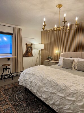Ein Hotelzimmer mit einem großen Bett, einer Bär-Dekoration, einem Schreibtisch mit einem Laptop, einem Fenster mit Vorhängen und einer Kristallleuchter.