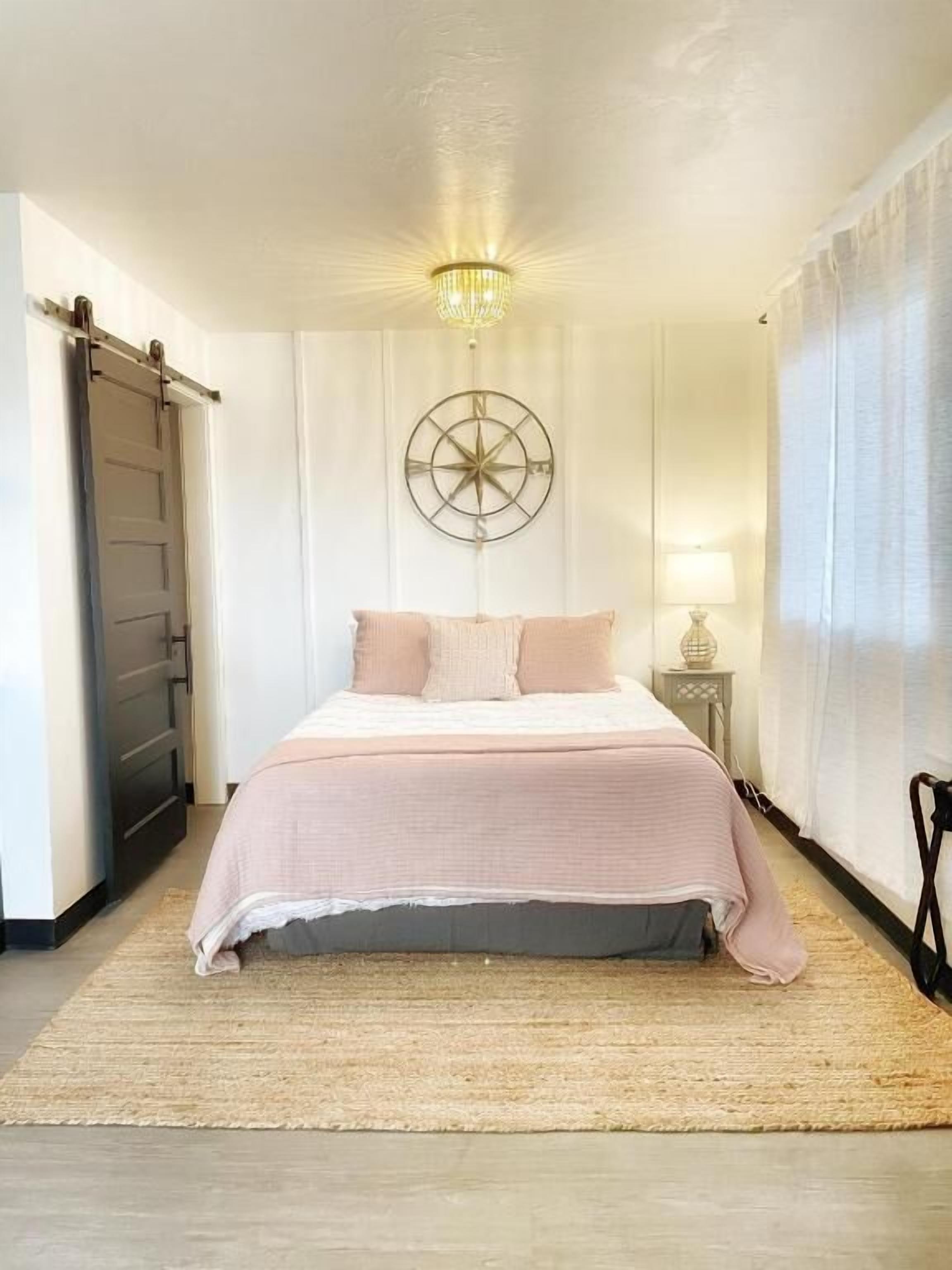 Una camera da letto con un letto, una decorazione a bussola appesa al muro, una lampada a sospensione e una porta.