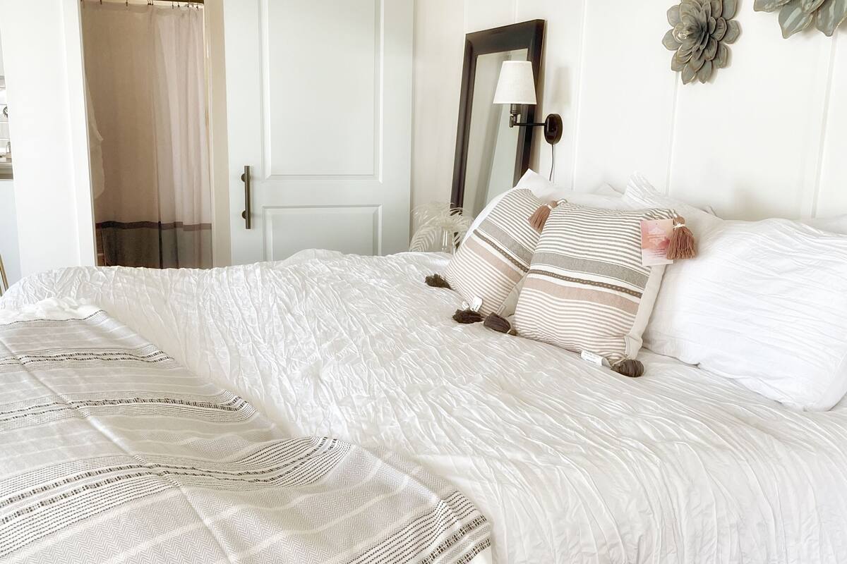 Ein Schlafzimmer mit Bett, Spiegel, Tür und einer Wandblume.