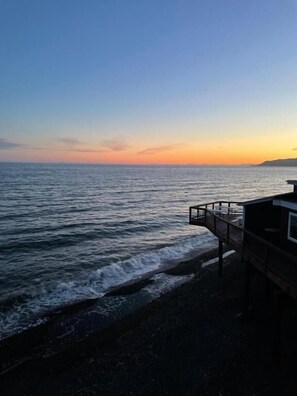 A coastal view with a wooden pier leading to a building with a bar area. - The Shack Inn (Homer)