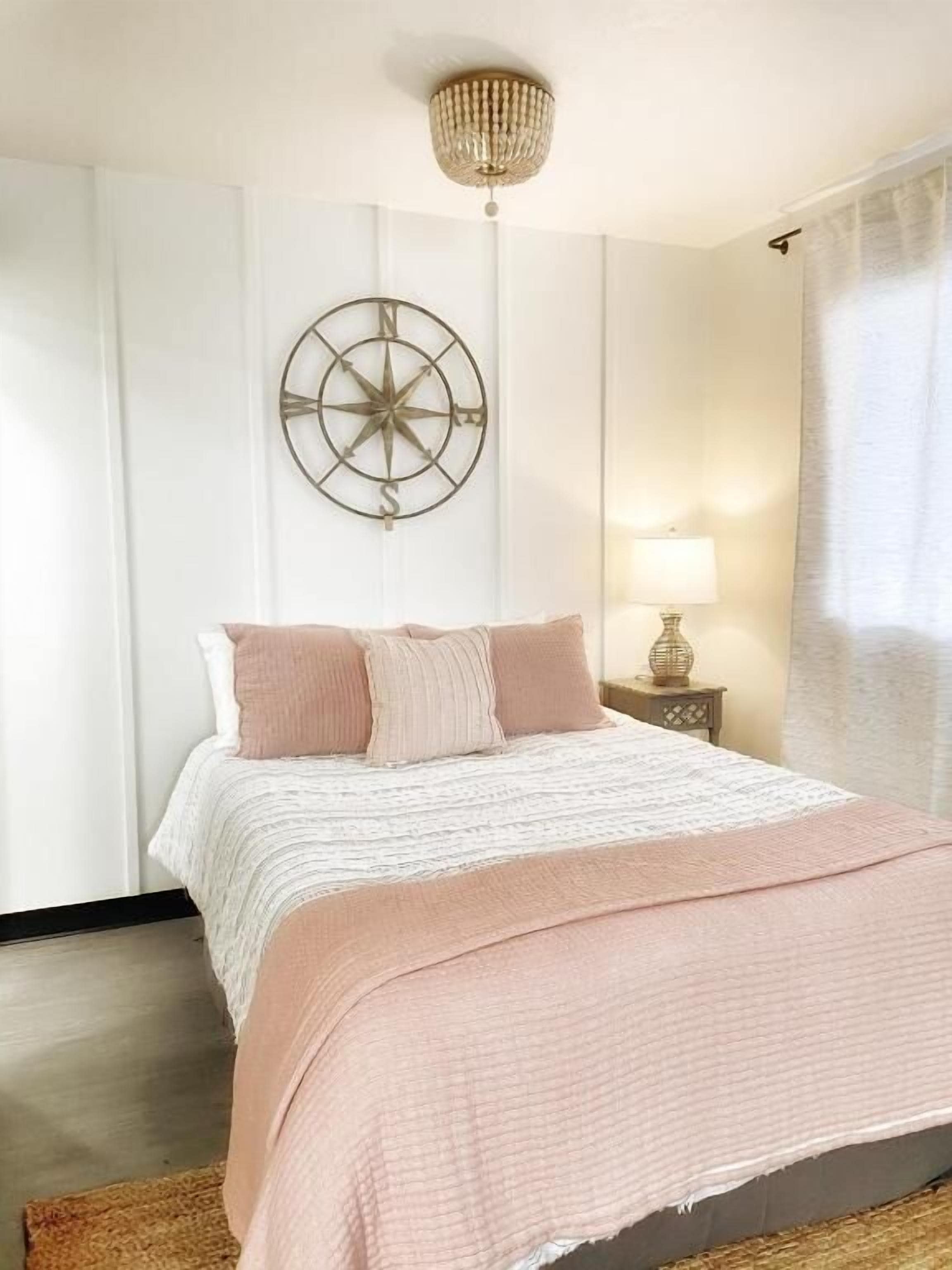 A neatly arranged bedroom with a bed, a wall-mounted compass decoration, a bedside lamp, and a window with curtains.