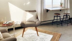 Ein modernes Wohnzimmer mit Sofa, Couchtisch, Wandfernseher, Fenster mit Vorhängen und einem kleinen Tisch mit Hockern.