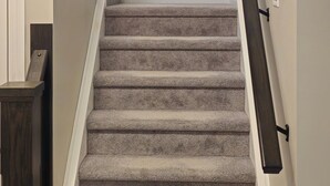A carpeted staircase with a handrail, a wooden handrail on the left, and a wall-mounted handrail on the right.