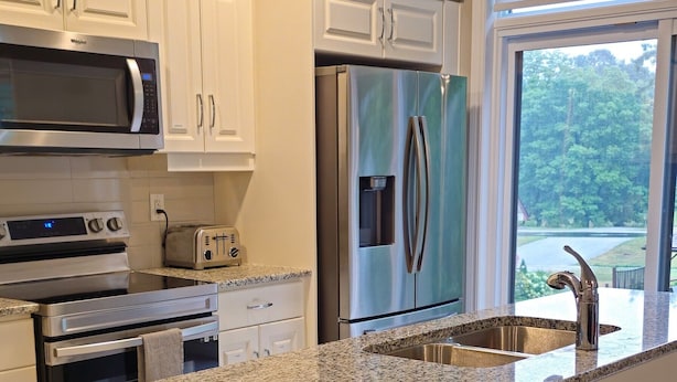 A kitchen with white cabinets, a granite countertop, stainless steel appliances, and a large island.