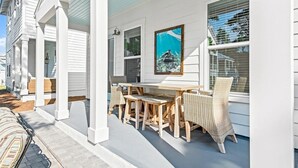 A covered porch with a wooden table and wicker chairs, white siding, and a framed picture of an underwater scene. - Beautiful 30A Beach House - short walk to beach! (Santa Rosa Beach)