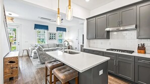 A modern kitchen with a central island, dark cabinetry, and a large window providing natural light. - Beautiful 30A Beach House - short walk to beach! (Santa Rosa Beach)