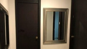 Un couloir avec deux portes sombres, un banc blanc et un miroir au mur.