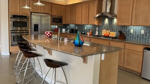 A modern kitchen with granite countertops, stainless steel appliances, wooden cabinets, and bar stools. - Colorful Artist’s Mansion w. pool and spa, pet friendly, all utilities included (Palm Springs)