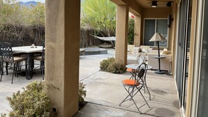 A covered patio area with outdoor furniture, including a table and chairs, and a seating area with sofas and a lamp. - Colorful Artist’s Mansion w. pool and spa, pet friendly, all utilities included (Palm Springs)