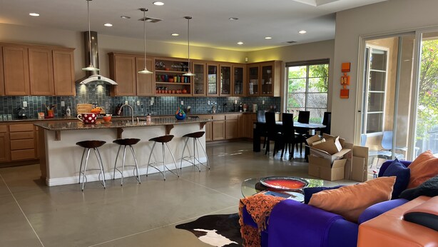 A modern kitchen with a central island, bar stools, and a dining area with a glass table. - Colorful Artist’s Mansion w. pool and spa, pet friendly, all utilities included (Palm Springs)