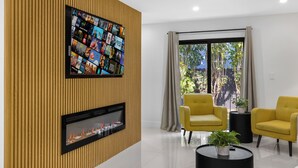 A modern living room with a flat-screen TV mounted on a wooden wall, a fireplace, yellow armchairs, and a large window with a view of greenery. - 5 BEDS / SLEEP 8 in a Prime Location in Miami! Near Airport/Cruise Terminal!  (Miami)