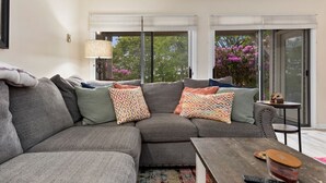 A modern living room with a grey sectional sofa, patterned throw pillows, a wooden coffee table, and a small side table.