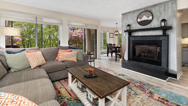 A living room with a fireplace, a sofa, a coffee table, and a view of the outdoors.