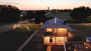 A two-story house with a balcony, surrounded by a well-lit driveway and a grassy area. - Group Spa All Day. Connect All Night. Near WinStar. (Thackerville)
