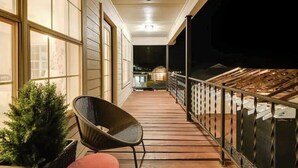 A wooden deck with a chair and potted plant, leading to a balcony with a railing and a view of the night sky. - Group Spa All Day. Connect All Night. Near WinStar. (Thackerville)