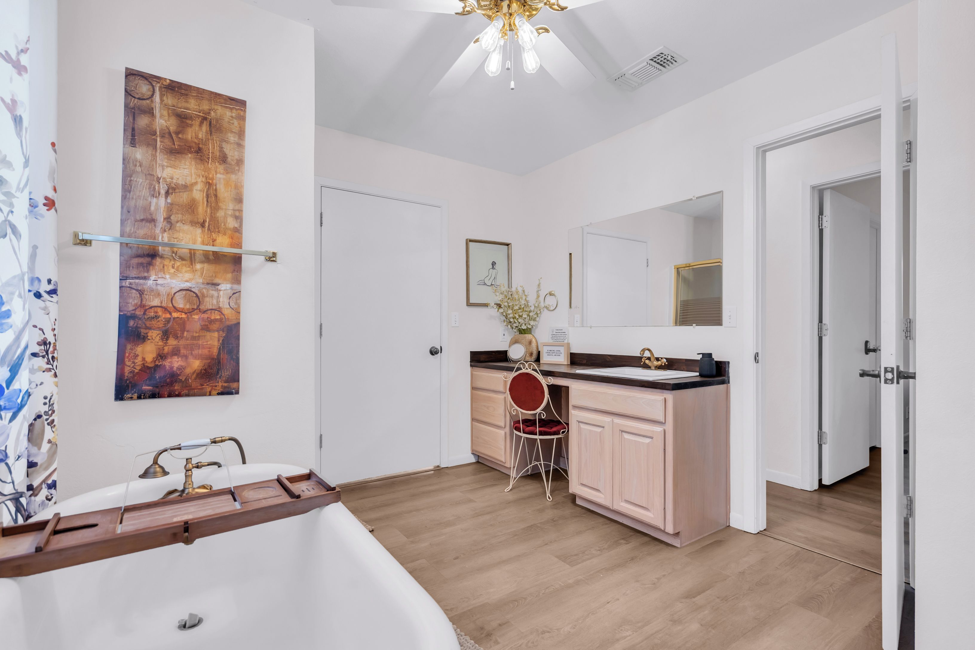 Un baño moderno con una bañera independiente, un tocador con espejo y suelo de madera.