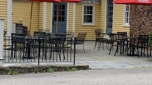 An outdoor patio area with tables and chairs, red umbrellas, and a yellow building with a gray roof. - The General Stanton Inn (Charlestown)