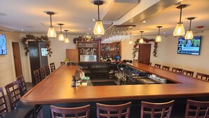 A bar area with a long wooden counter, multiple bar stools, hanging light fixtures, and a television screen mounted on the wall. - The General Stanton Inn (Charlestown)