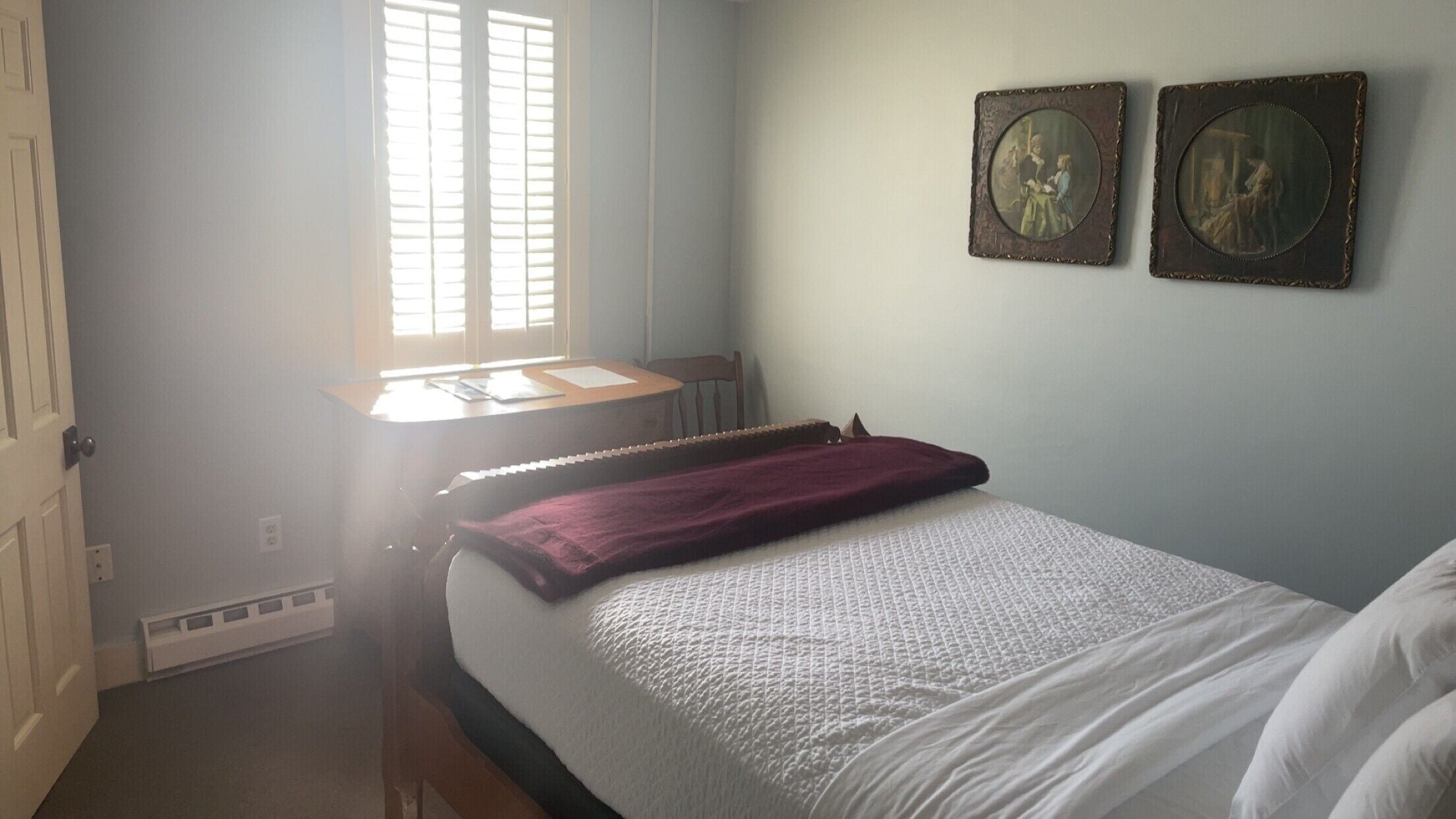 A bedroom with a bed, a desk, and two wall-mounted picture frames.